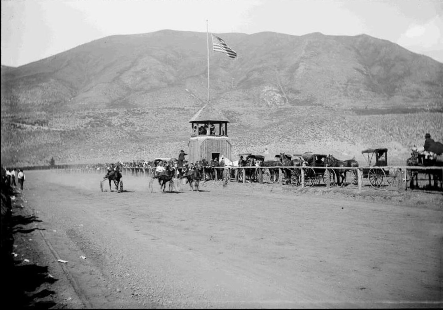 One b/w glass-plate negative of a horse race. There is the bandstand with the announcers and a flag on top, horse and buggies on side with the spectators as well as th horse drawn carts on the race track. Red Mountain is in the background. The horse track was in the west end where the Aspen Meadows is (2007). Courtesy of the Aspen Historical Society.