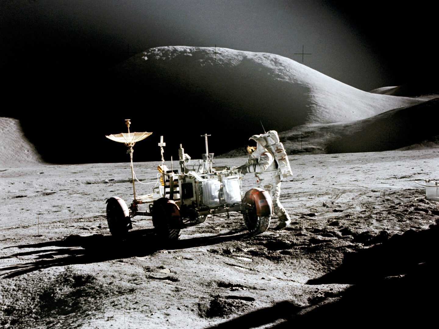 Apollo Astronaut James B. Irwin, lunar module pilot, works at the Lunar Roving Vehicle during the first Apollo 15 lunar surface extravehicular activity (EVA) at the Hadley-Apennine landing site. The shadow of the Lunar Module "Falcon" is in the foreground. This view is looking northeast, with Mount Hadley in the background. This photograph was taken by astronaut David R. Scott, commander. Image Credit: NASA